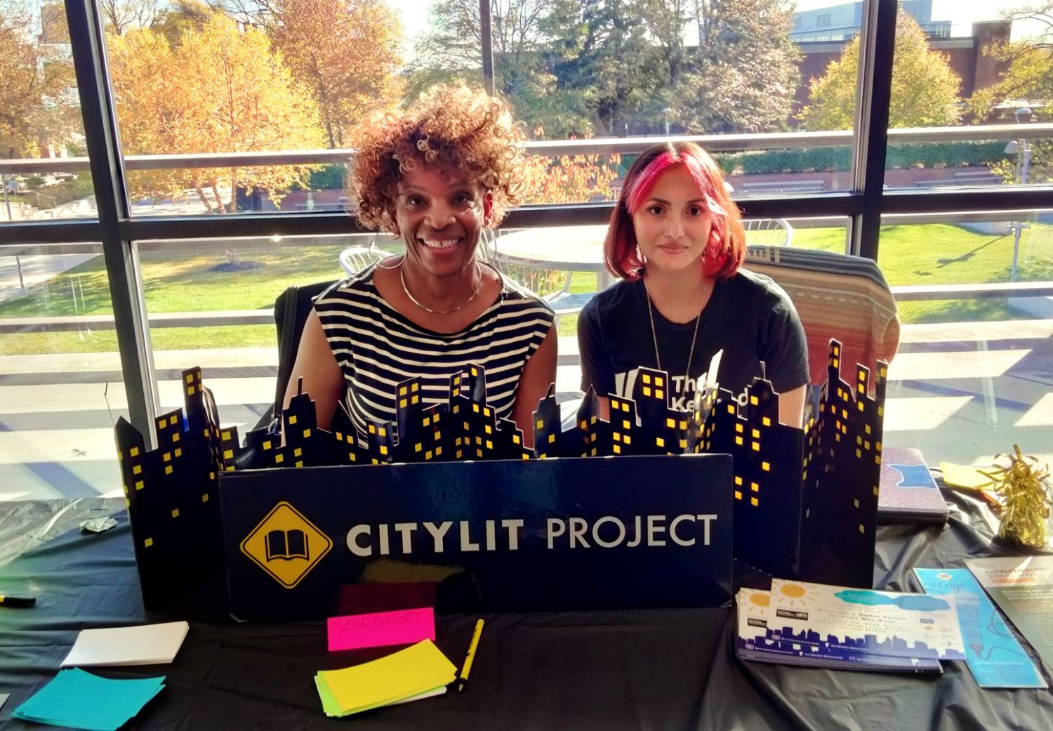 Cherrie Woods and Lillian Jacobson sit at the CityLit Project table in front of a large window